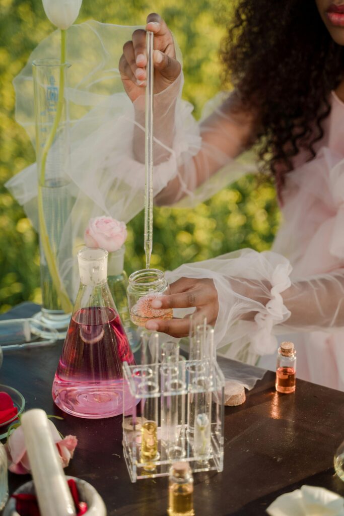 pexels-photo-10536307-10536307 A woman with curly hair mixing perfumes outdoors with glassware and pipette.