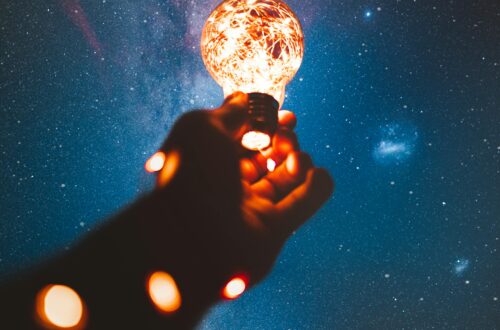 A hand holds a glowing bulb into the Milky Way night sky, creating a magical cosmic connection.