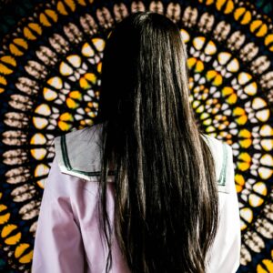 žena s dlouhými tmavými vlasy stojí před živým pozadím s mandalovým vzorem, což vytváří výrazný vizuální kontrast.