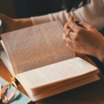 Žena píše do deníku, zatímco si vychutnává šálek kávy u dřevěného stolu.