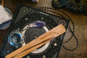 Astrologie znamená "věda o hvězdách" – i když moderní astronomie by se u toho trochu otřásla. astrologická tematika, deska na kterém je kniha o datu narození, krystaly a náhrdelník na dřevěném povrchu.