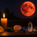 Krvavý úplněk v Rybách za oknem, zapálená svíčka a minerály – citrín, malachit, růženín, safír a křišťál._Blood Moon in Pisces with candle and crystals (citrine, malachite, rose quartz, sapphire, clear quartz)._Blutmond in den Fischen mit Kerze und Edelsteinen (Citrin, Malachit, Rosenquarz, Saphir, Bergkristall).