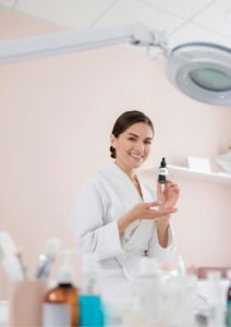 -Krásná žena v županu, která drží lahvičku séra a usmívá se v estetickém prostředí lázní. -Beautiful woman in a bathrobe holding a serum bottle, smiling in an aesthetic spa setting. - Schöne Frau im Bademantel, die eine Serumflasche hält und in einer ästhetischen Spa-Umgebung lächelt.