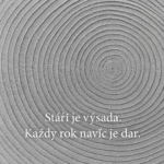 Detailní černobílá fotografie letokruhů dřeva. Viditelné soustředné kruhy symbolizují roky a růst. V obrázku je umístěný nápis „Stáří je výsada. Každý rok navíc je dar.“