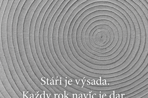 Detailní černobílá fotografie letokruhů dřeva. Viditelné soustředné kruhy symbolizují roky a růst. V obrázku je umístěný nápis „Stáří je výsada. Každý rok navíc je dar.“