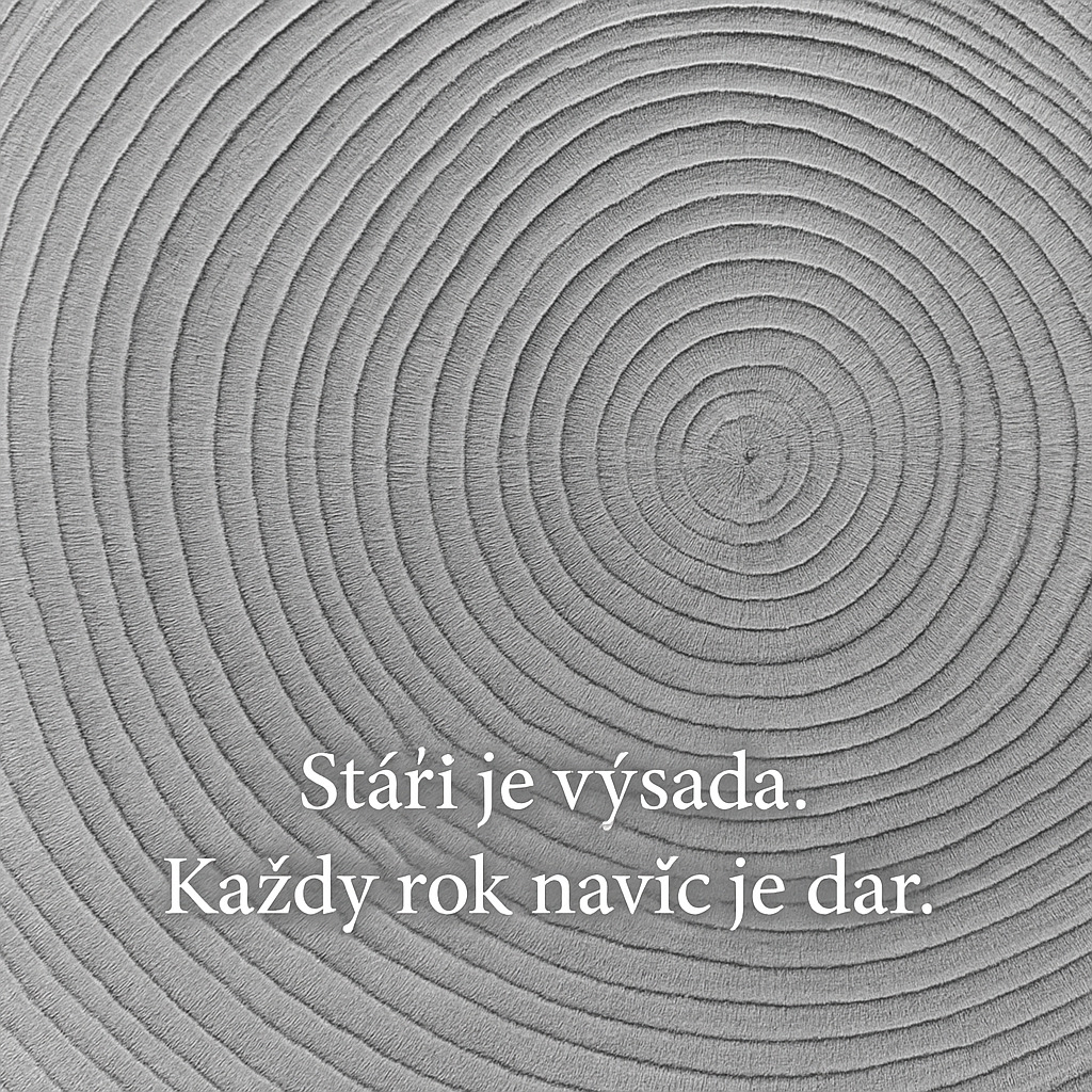 Detailní černobílá fotografie letokruhů dřeva. Viditelné soustředné kruhy symbolizují roky a růst. V obrázku je umístěný nápis „Stáří je výsada. Každý rok navíc je dar.“