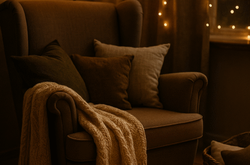 „Zimní koutek s ušákem, měkkou dekou, polštáři a zapálenou svíčkou, v teplém světle lampy a jemných světýlek v pozadí.“ Popisek pod obrázek