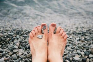 pexels-photo-1274061-1274061 Close-up of female feet with stones on pebbled beach by the water, evoking relaxation and tranquility.