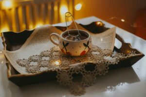 Hygge je dánské slovo, které označuje stav útulnosti, pohody a spokojenosti, často spojený s uměním užívat si drobné radosti v příjemné atmosféře. Warm and inviting tea arrangement with a decorated teacup and lace on a wooden tray, perfect for cozy moments.