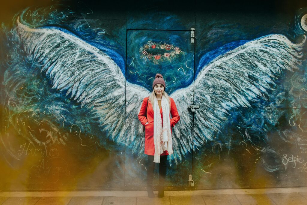 Woman posing in front of angel wings street art in Bangor, Wales. Říká se, že poslední noc v roce je kouzelná a co si upřímně přejete, to se splní. Nechte si tuto noc pro své sny.