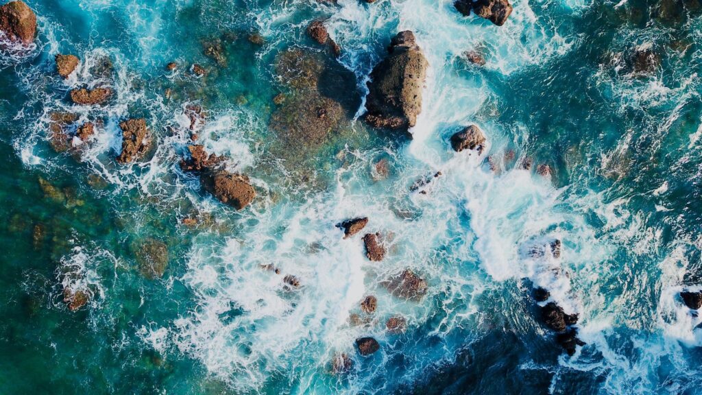 Stunning aerial view of ocean waves crashing against rocks, creating a beautiful natural pattern.
