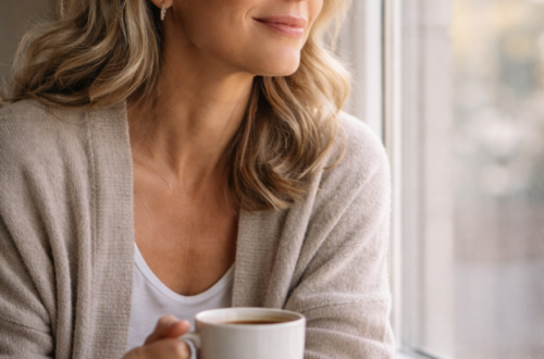 Žena 50+ sedí u okna s hrnkem kávy v ranním denním světle, bez výrazného make-upu, klidný výraz a přirozená pleť. Někdy je největší luxus klid.