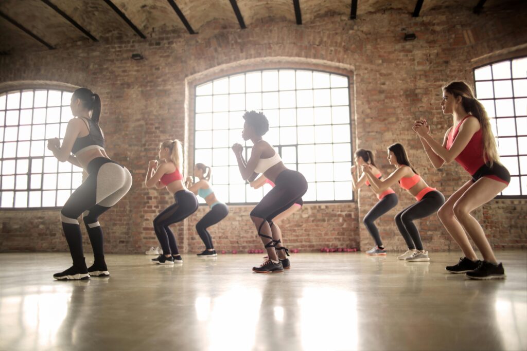 Dřep (Squat) participating in a group fitness class performing squats in an industrial-style studio.
