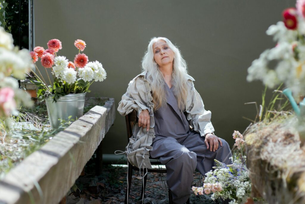 Serene elderly woman surrounded by colorful blooms outdoors, showcasing grace and nature's beauty.