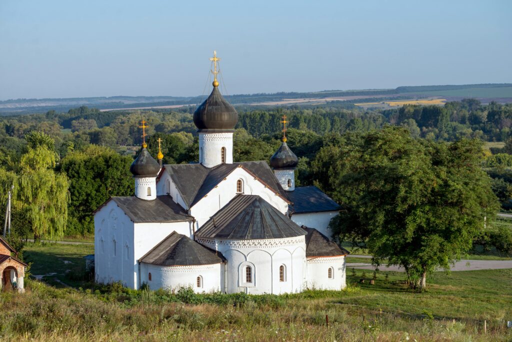 Aerial shot of a white Orthodox church amidst lush green landscape under a clear sky.