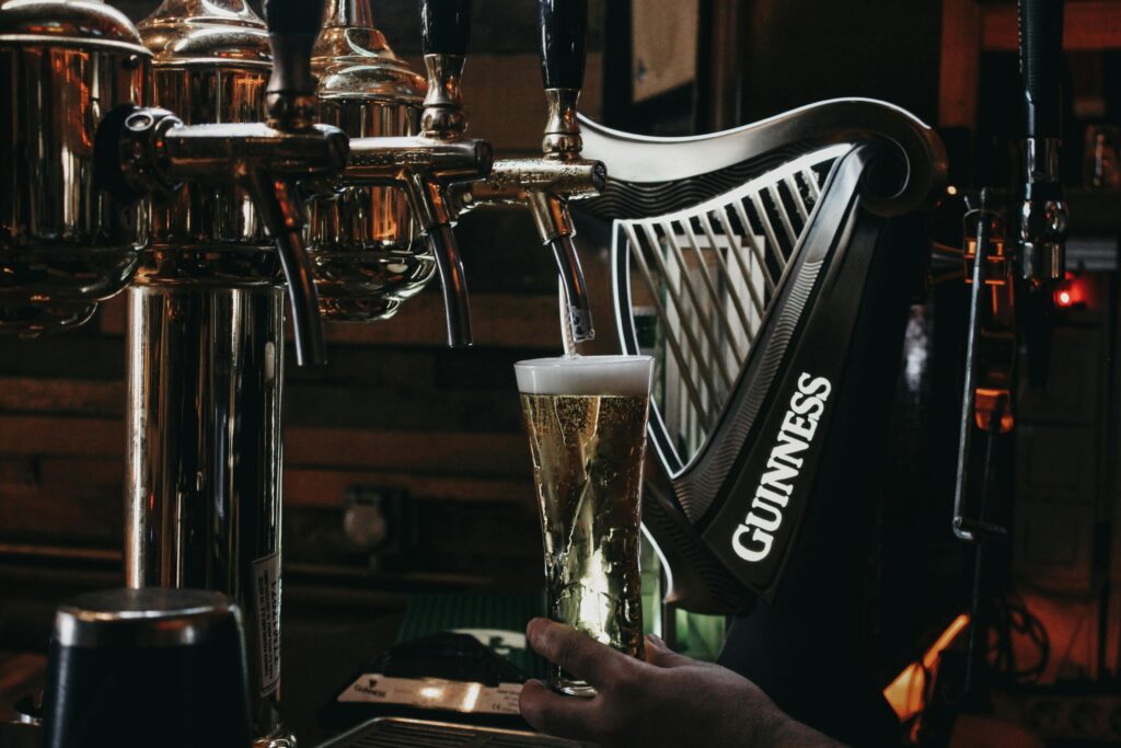 Guinness,, irské pivo, znak Irska - harfa, A refreshing glass of lager being poured from a stylish pub beer tap.