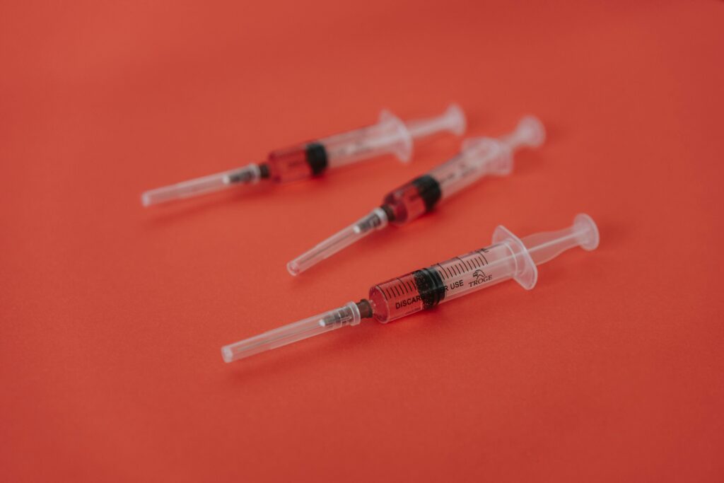 Ozempic, Mounjaro a spol., chemický diktát, Three syringes with red liquid on a bold red surface, featuring medical themes.