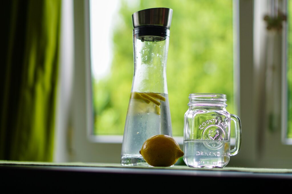 hydratace, voda s citronem, karfa s vodou, Lemon-infused water in a glass carafe and mason jar on a windowsill, evoking freshness.