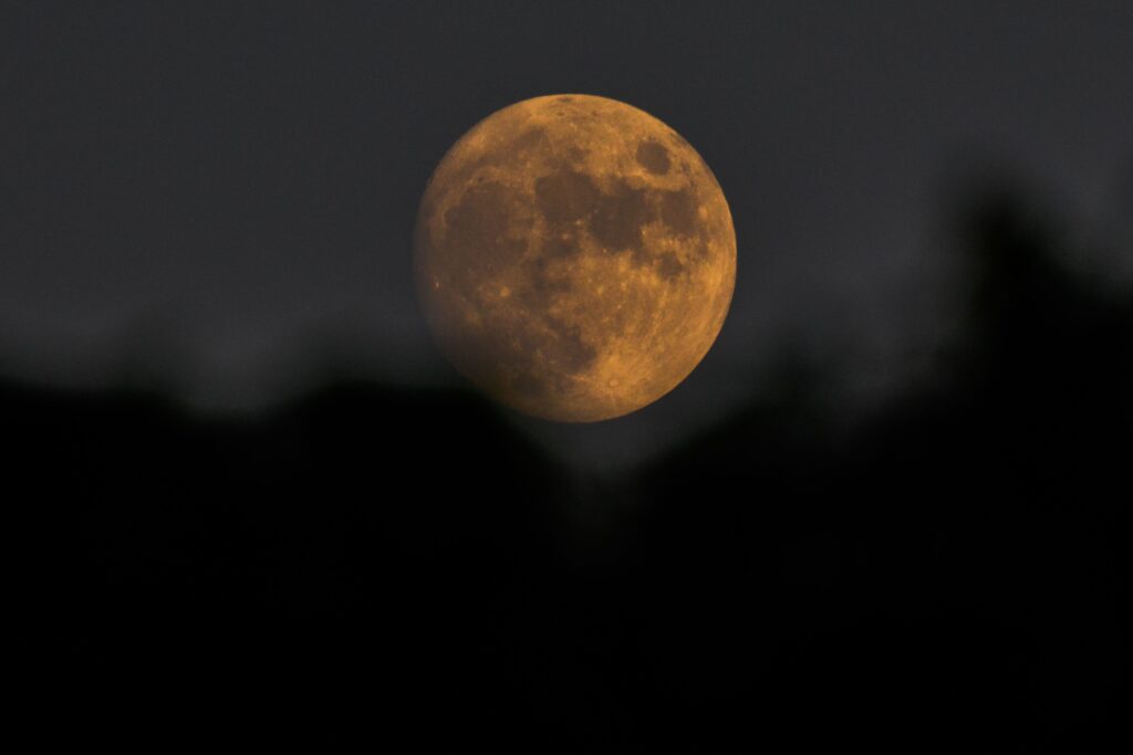 jelení úplněk, astronomie, úplněk, A striking full moon with a warm golden hue set against a dark, cloudy night sky.