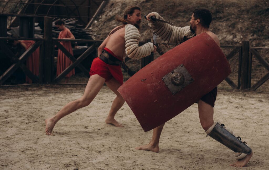 tRIBALISMUS, HÁDKY, KMEN, Two gladiators engaged in intense combat in a historical arena setting.