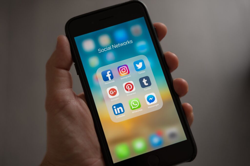 Mobil, sociální sítě, algoritmus, A smartphone displaying various social media icons held in a hand, showcasing modern communication apps.