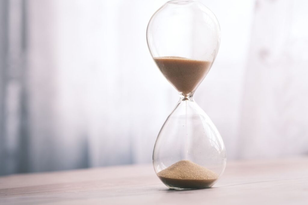 Time, vymezený čas, konečnost, chvíle, moment, Minimalist hourglass filled with sand symbolizing time and patience, against a soft background.